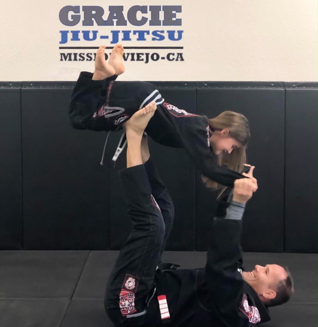 Professor Bob lifting a young student under the Gracie Jiu-Jitsu Mission Viejo sign