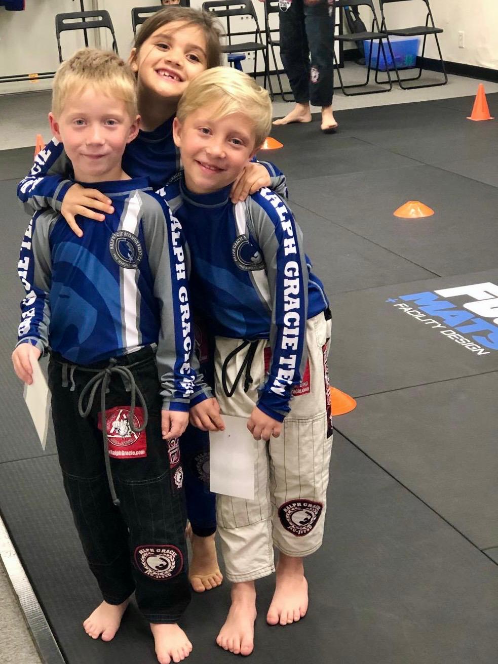 Three young Mission Jiu Jitsu teammates smiling on the mats